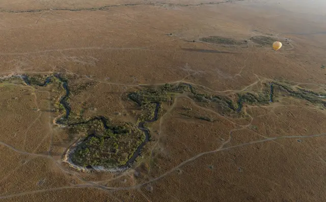 Aerial view of the winding Mara River with a balloon on the horizon