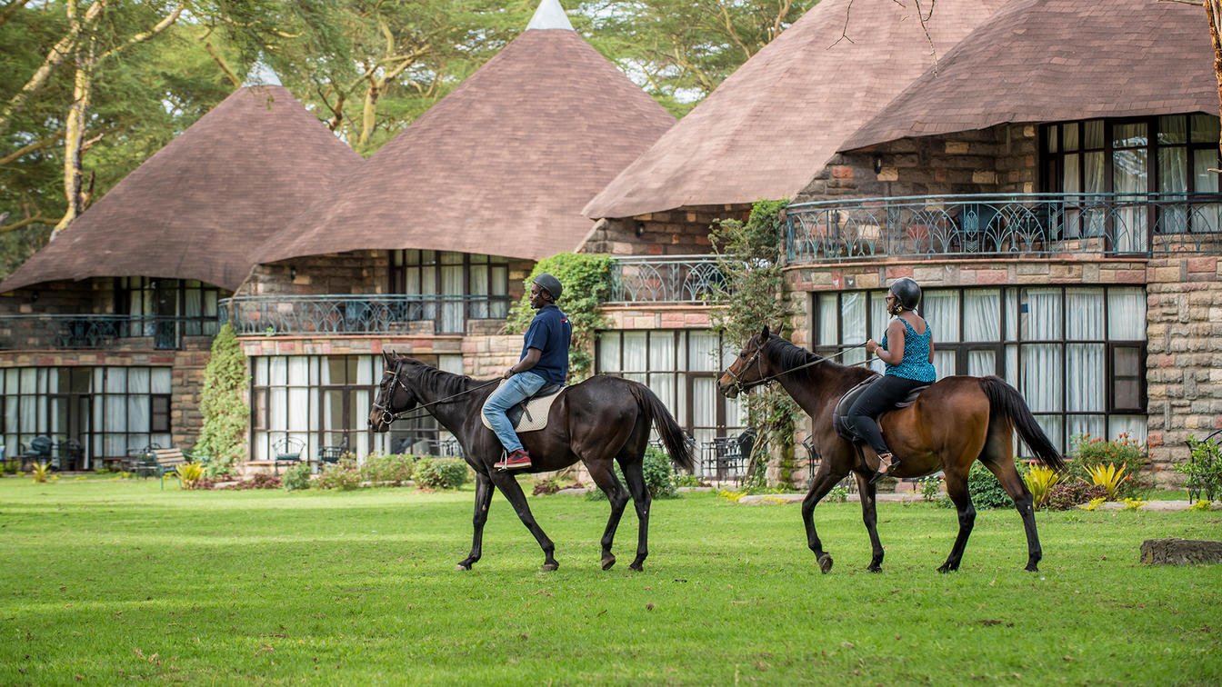 Guests horse riding past thatched cottages at Lake Naivasha Sopa Lodge