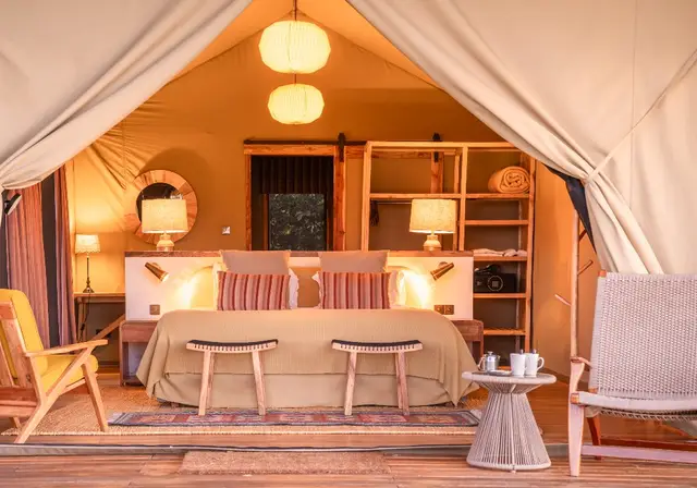 Warmly lit interior of a Governors' Camp family tent with twin beds and lanterns