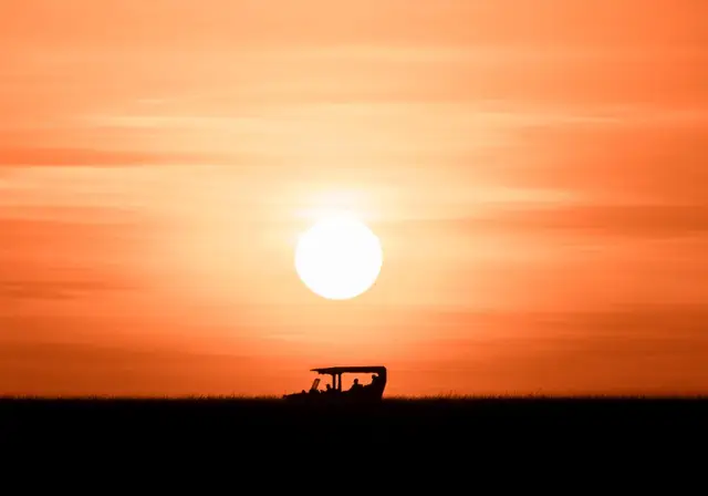 Safari vehicle silhouetted against a huge orange Masai Mara sunset