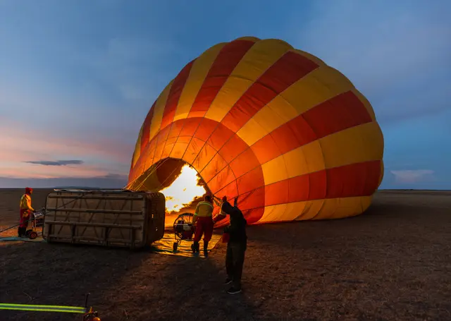 Crew inflating a hot-air balloon with a burner flame at dawn in the Maasai Mara